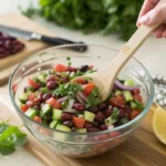 A colorful dense bean salad in a rustic ceramic bowl with fresh vegetables and vinaigrette dressing.